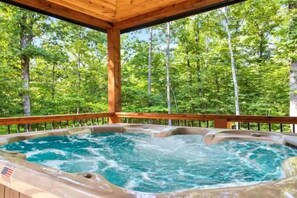 A hot tub with a wooden deck and a forest backdrop. - Hot Tub, Fire Pit, Ping Pong, Near Beavers Bend (Broken Bow)
