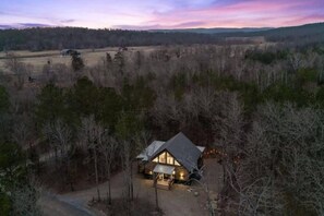 A single-story cabin with a sloped roof, surrounded by dense forest, and a clear view of the sky. - Hot Tub, Fire Pit, Ping Pong, Near Beavers Bend (Broken Bow)