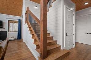 Una escalera de madera con barandilla, paredes de paneles blancos y una puerta con picaporte negro.