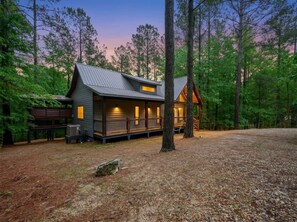 A cabin with a deck, surrounded by trees, and a clear sky. - Hot Tub, Soaking Tub & Fireplaces | King Suite (Broken Bow)