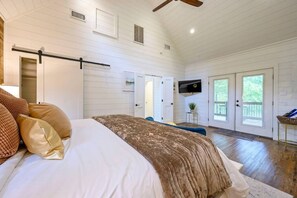 Un dormitorio con cama, almohadas, televisor y una puerta que da a un balcón.