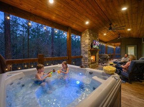 A hot tub area with a stone fireplace and a deck overlooking a forest. - Hot Tub, Soaking Tub & Fireplaces | King Suite (Broken Bow)