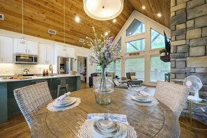 A modern kitchen with white cabinets, stainless steel appliances, and a dining area with a wooden table set for four. - Hot Tub, Soaking Tub & Fireplaces | King Suite (Broken Bow)