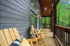 A wooden deck with a rocking chair and a bench, overlooking a forested area. - Hot Tub, Soaking Tub & Fireplaces | King Suite (Broken Bow)