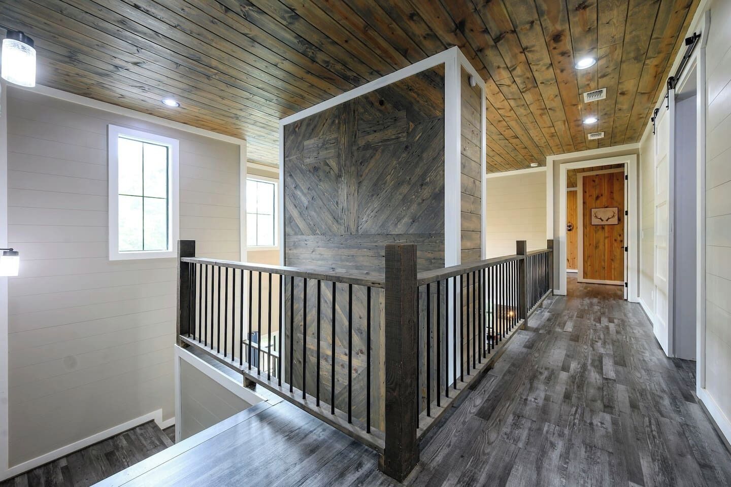 A spacious hallway with a wooden floor, a railing, and a large wooden accent wall.