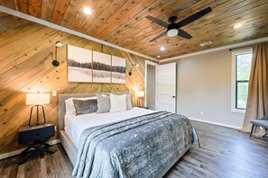 A bedroom with a sloped ceiling, a bed with a grey blanket, two bedside lamps, and a ceiling fan. - Heated Pool, Hot Tub, Game Room - Sleeps 24 (Broken Bow)
