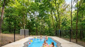 Ein Schwimmbecken mit Steinbord, umgeben von einem schwarzen Zaun und Bäumen im Hintergrund.