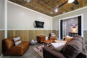 A living room with leather sofas, a wooden ceiling, a mounted TV, and a door leading to another room. - Heated Pool, Hot Tub, Game Room - Sleeps 24 (Broken Bow)