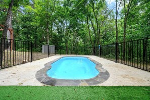 A rectangular swimming pool with a stone edge, surrounded by a black metal fence, set in a grassy area with trees in the background. - Heated Pool, Hot Tub, Game Room - Sleeps 24 (Broken Bow)