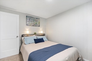 A bedroom with a bed, a nightstand, a lamp, a door, and a wall-mounted painting.