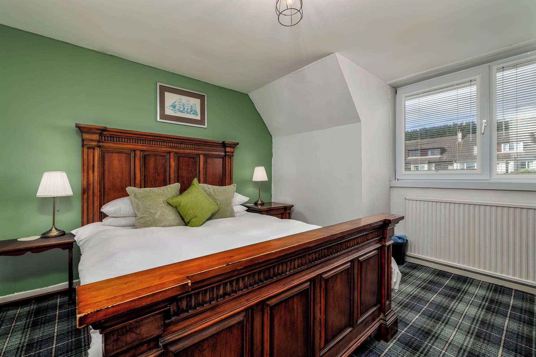 Quarto com cama de madeira, paredes verdes, janela com persianas e radiador.