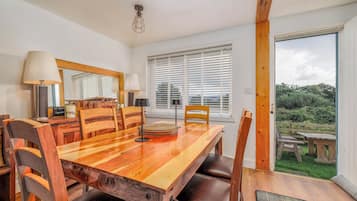 Un comedor con una mesa de madera, sillas y vistas al exterior a través de amplios ventanales.