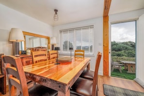 A dining area with a wooden table, chairs, and a view of the outdoors through large windows.
