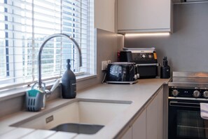 A modern kitchen with a built-in oven, a stovetop, and a window with blinds.