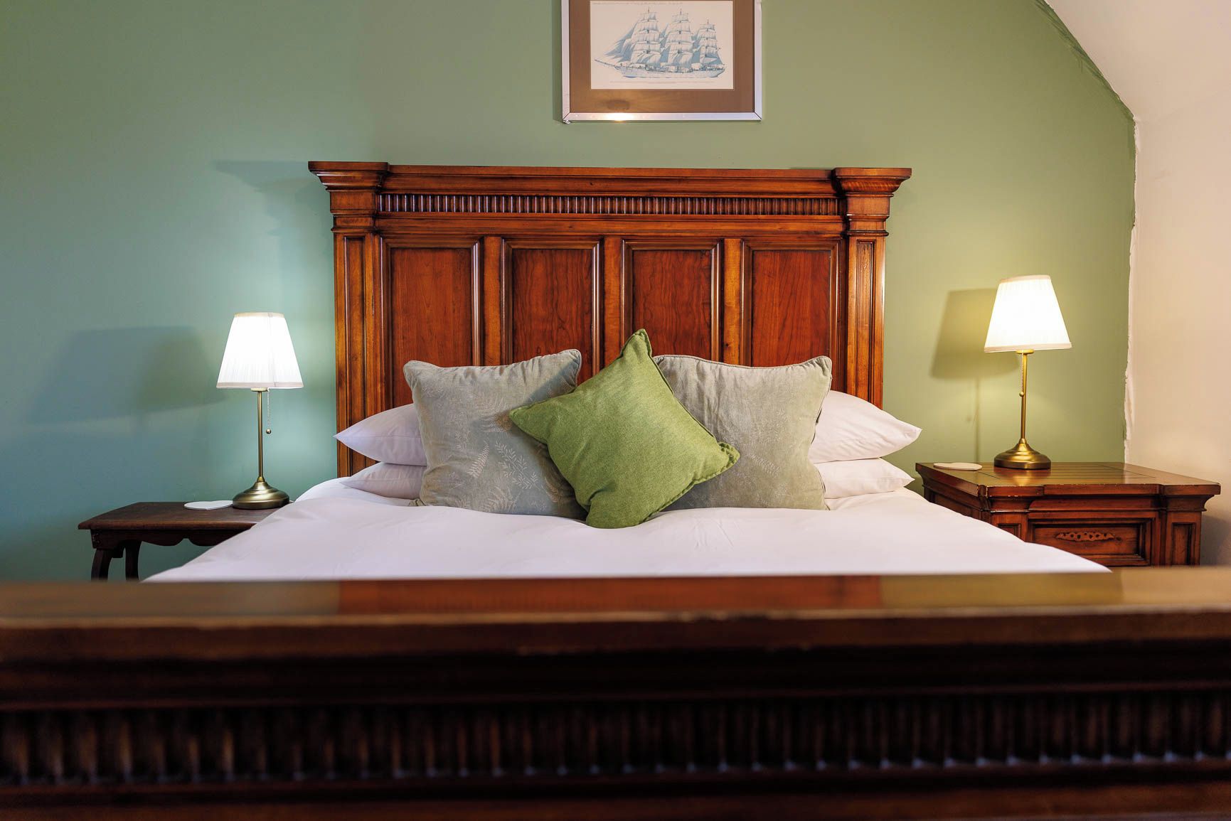 A neatly made bed with a wooden headboard, two bedside lamps, and a framed picture on the wall.