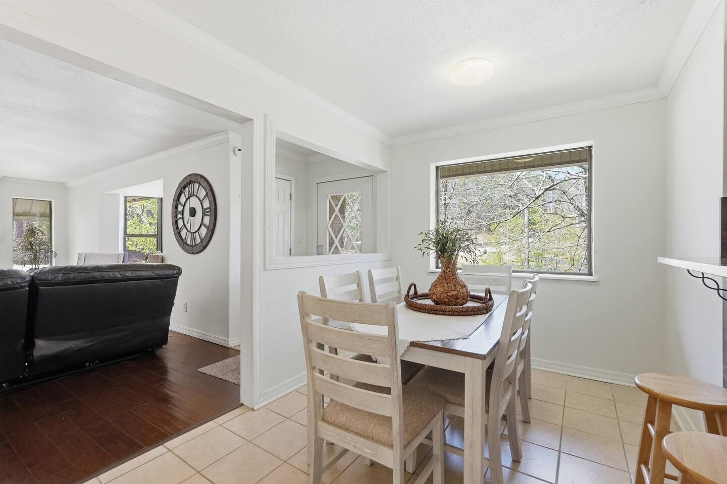 A dining area with a table, chairs, a clock, and a window with a view.