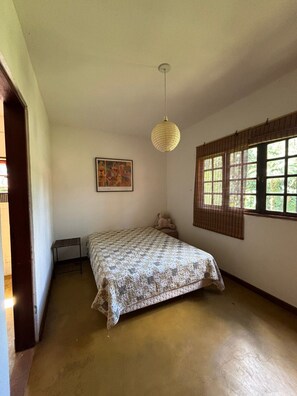 A room with a bed, a hanging light fixture, a window with blinds, and a framed picture on the wall. - Cozy property for the whole family. 50km from São Paulo. (Caucaia do Alto)