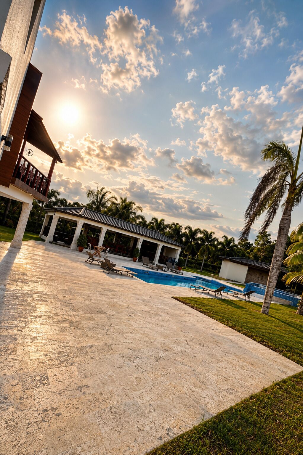 A resort with a swimming pool, lounge chairs, and a covered area with a view of the sunset.