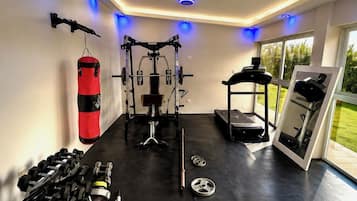 Ein Fitnessraum mit Trainingsgeräten, einem Boxsack und einem Laufband.