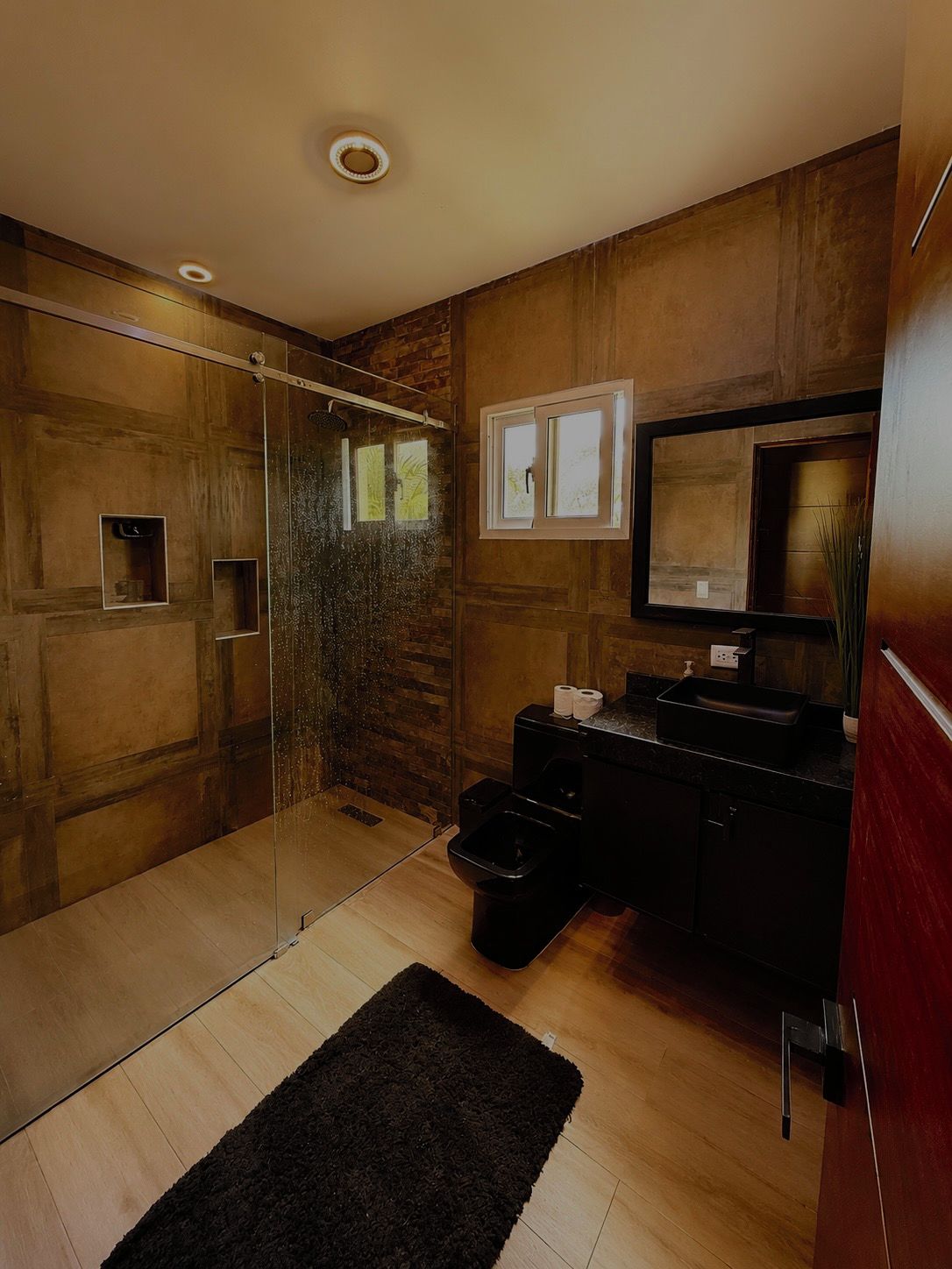 Ein modernes Badezimmer mit einer Glasdusche, Holzwänden, einem schwarzen Waschbecken und einem Spiegel.