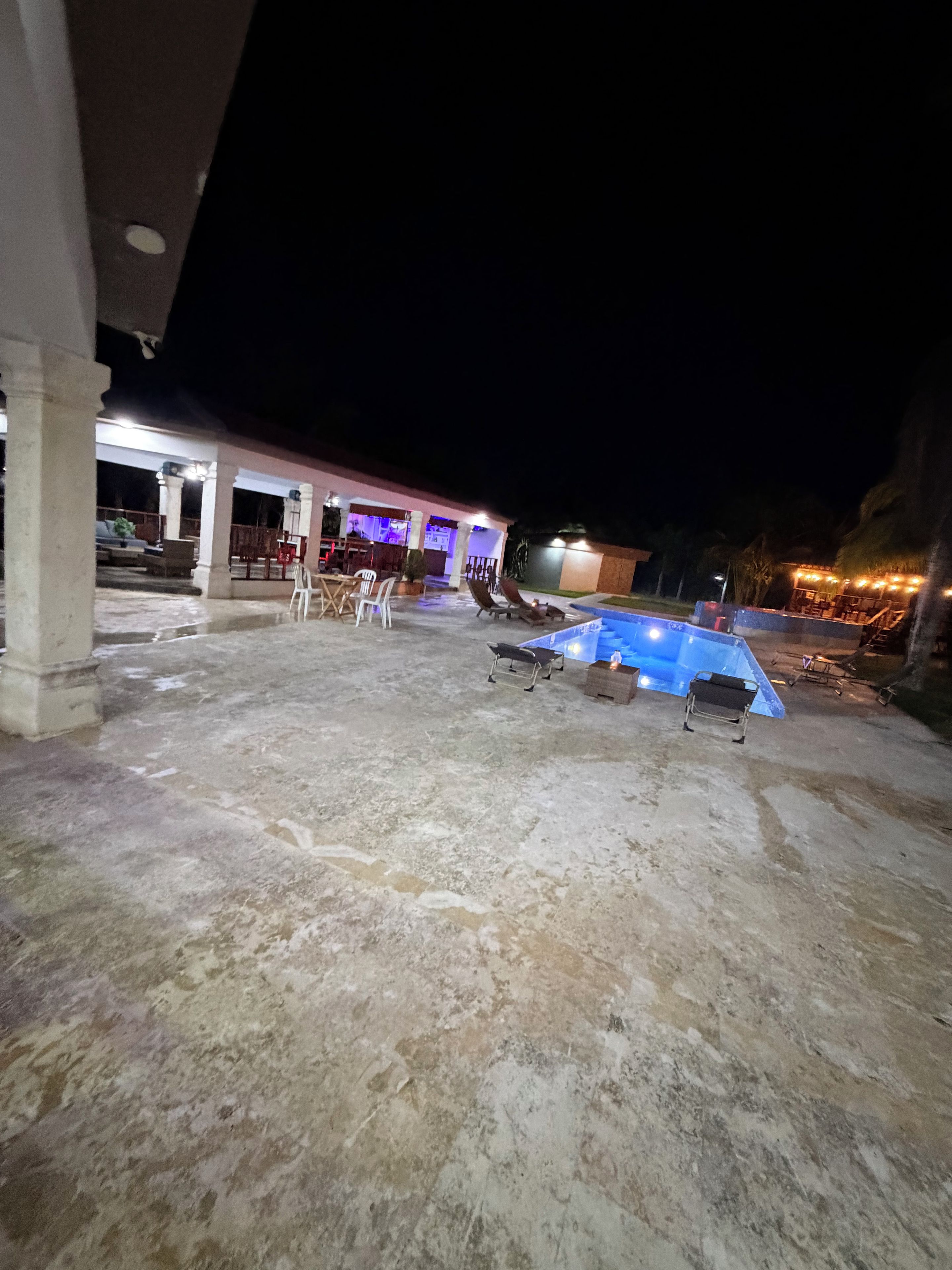 Zona de piscina exterior con sillones de descanso y un bar con iluminación.