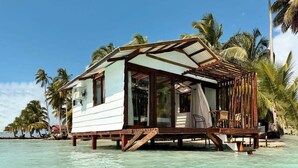 A bungalow-style overwater accommodation with a glass-enclosed porch, wooden deck, and a view of the turquoise sea.