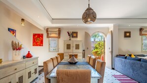 A spacious dining area with a long table, cushioned chairs, and a hanging light fixture.