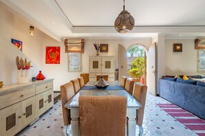 A spacious dining area with a long table, cushioned chairs, and a hanging light fixture.