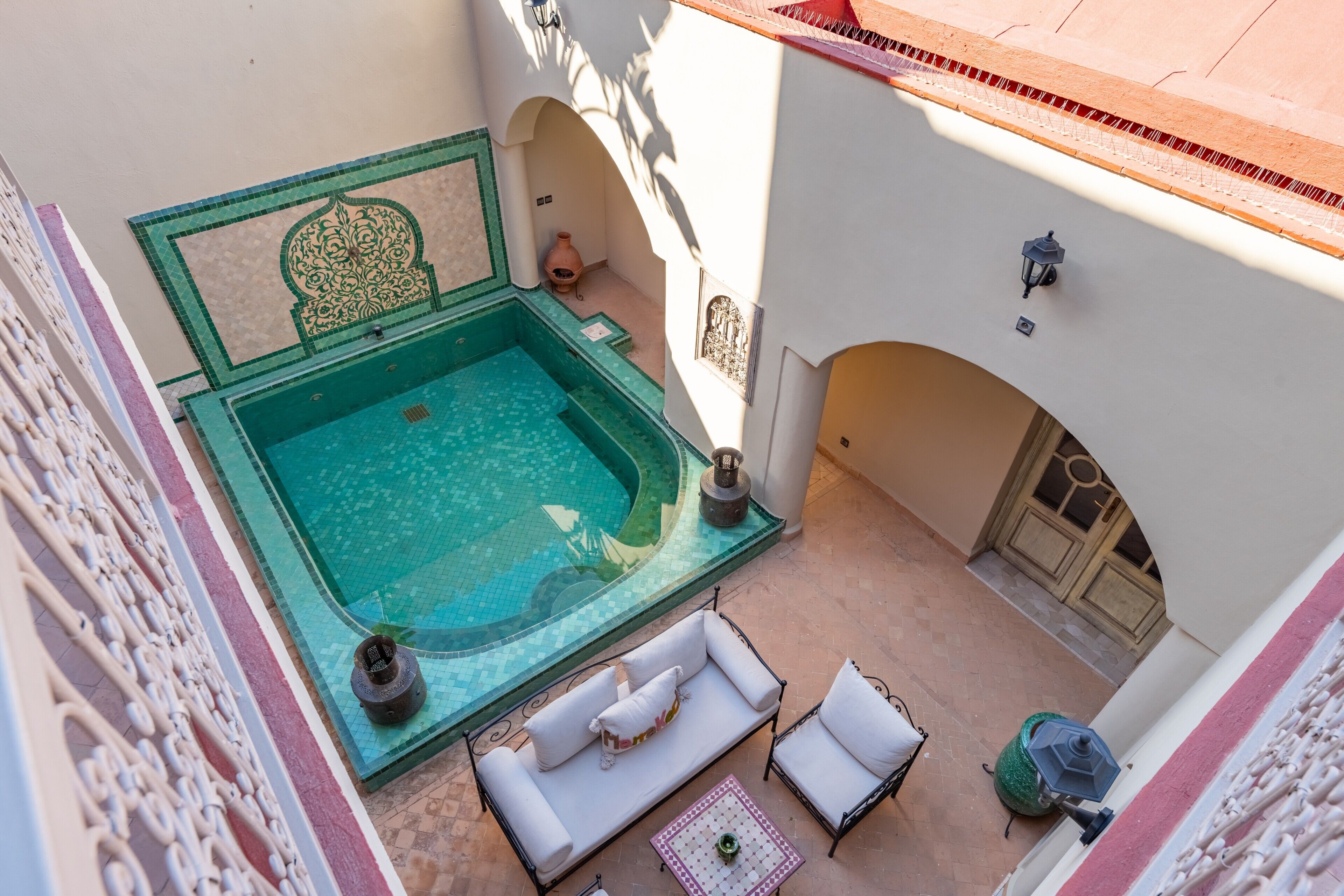 A rooftop pool with a jacuzzi, white outdoor furniture, and a decorative wall.