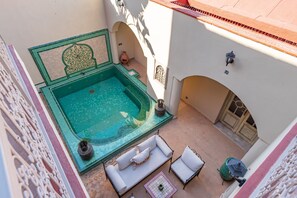 A rooftop pool with a jacuzzi, white outdoor furniture, and a decorative wall.