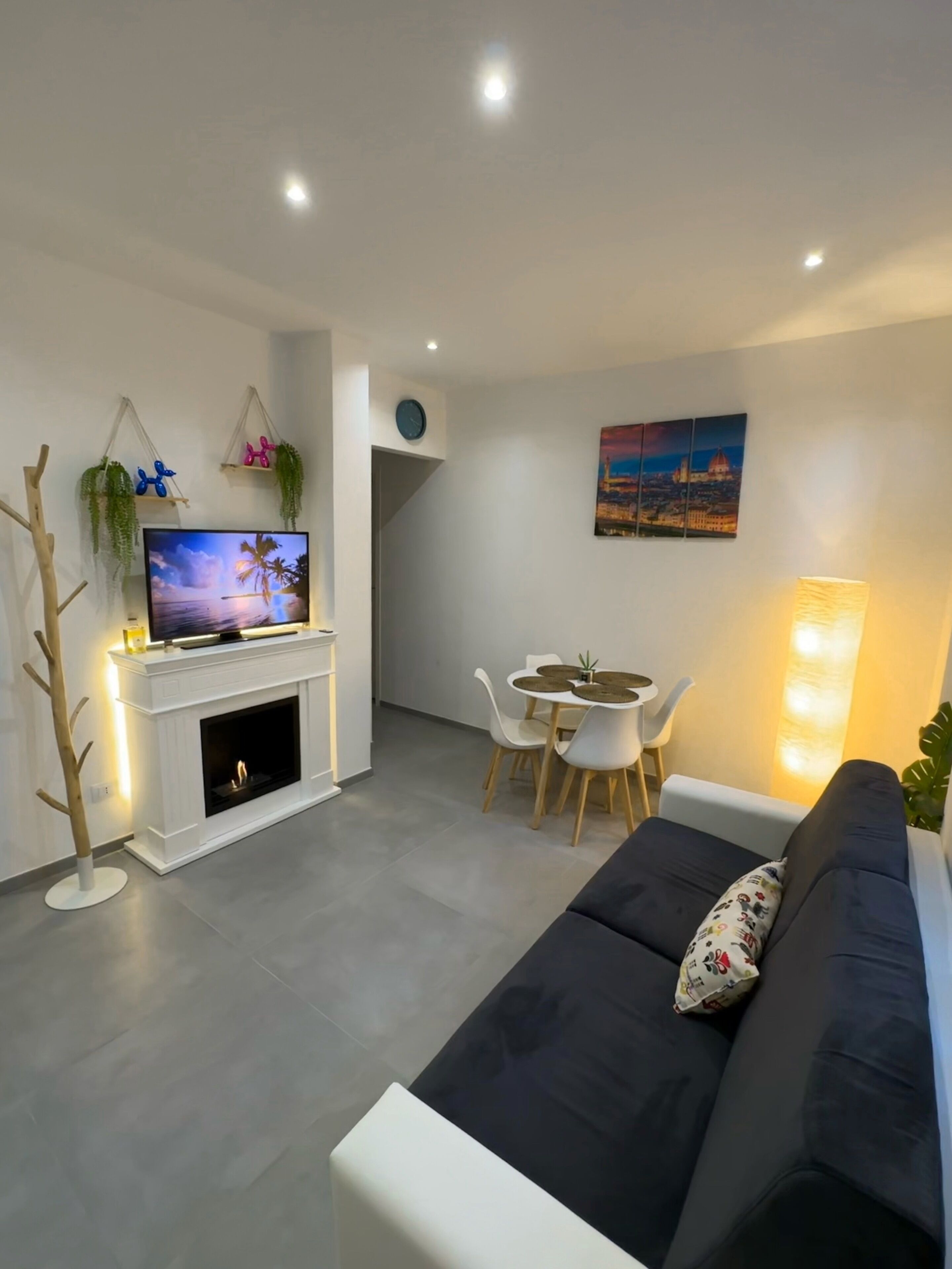 Una sala de estar moderna con chimenea, televisor de pantalla plana, comedor con mesa y sillas, y un sofá con un cojín decorativo.