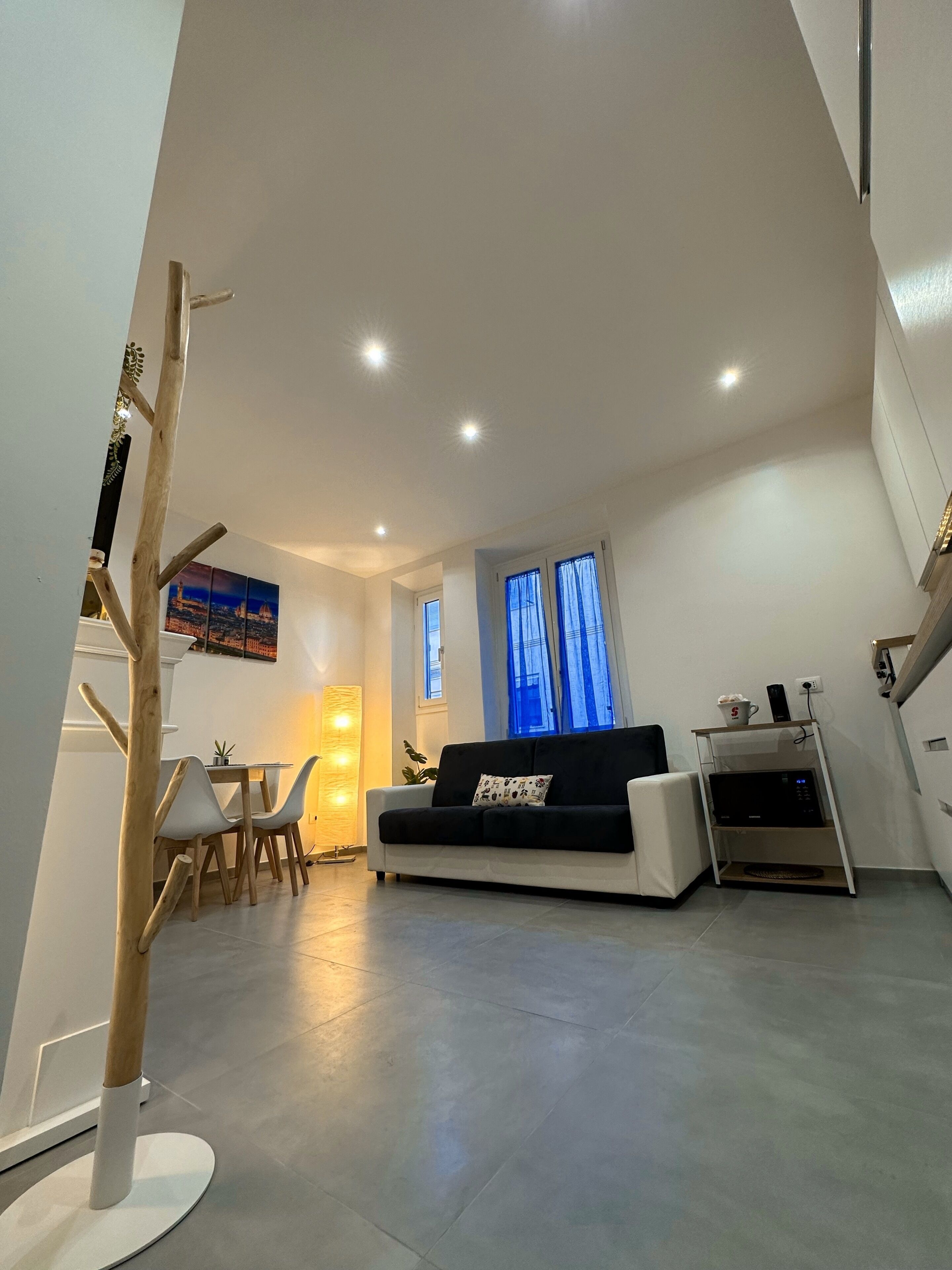 A modern living room with a sofa, dining table, and chairs. There is a staircase leading to an upper level.