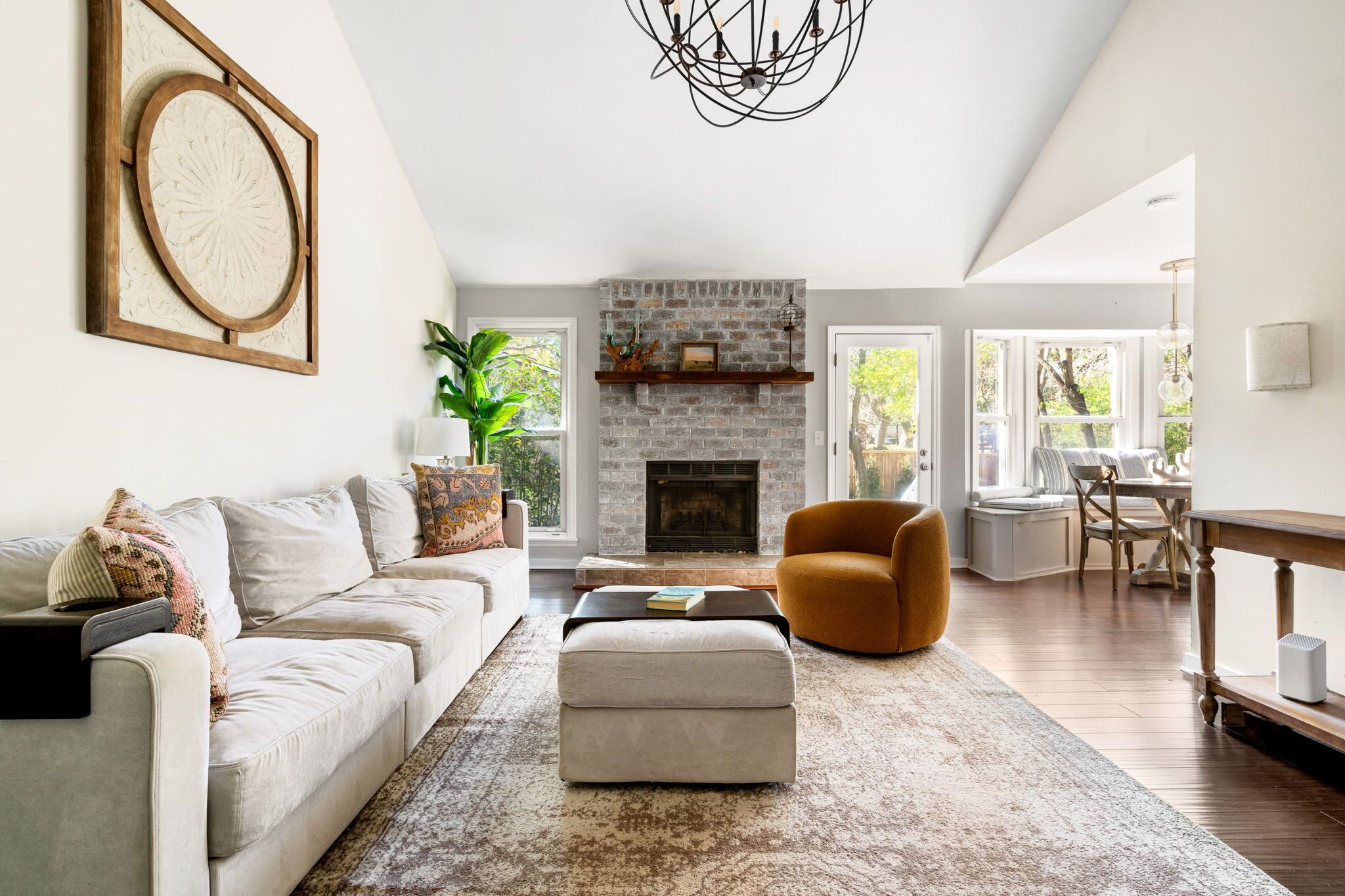 A spacious living room with a fireplace, a sofa, an ottoman, and a dining area with natural light.