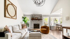 A spacious living room with a fireplace, a sofa, an ottoman, and a dining area with natural light. - Delightful 3-bedroom house in charming Charleston (Charleston)