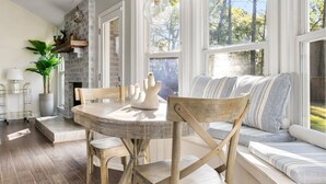 A dining area with a round table and chairs, a built-in bench with cushions, and a large window providing a view of the outdoors. - Delightful 3-bedroom house in charming Charleston (Charleston)