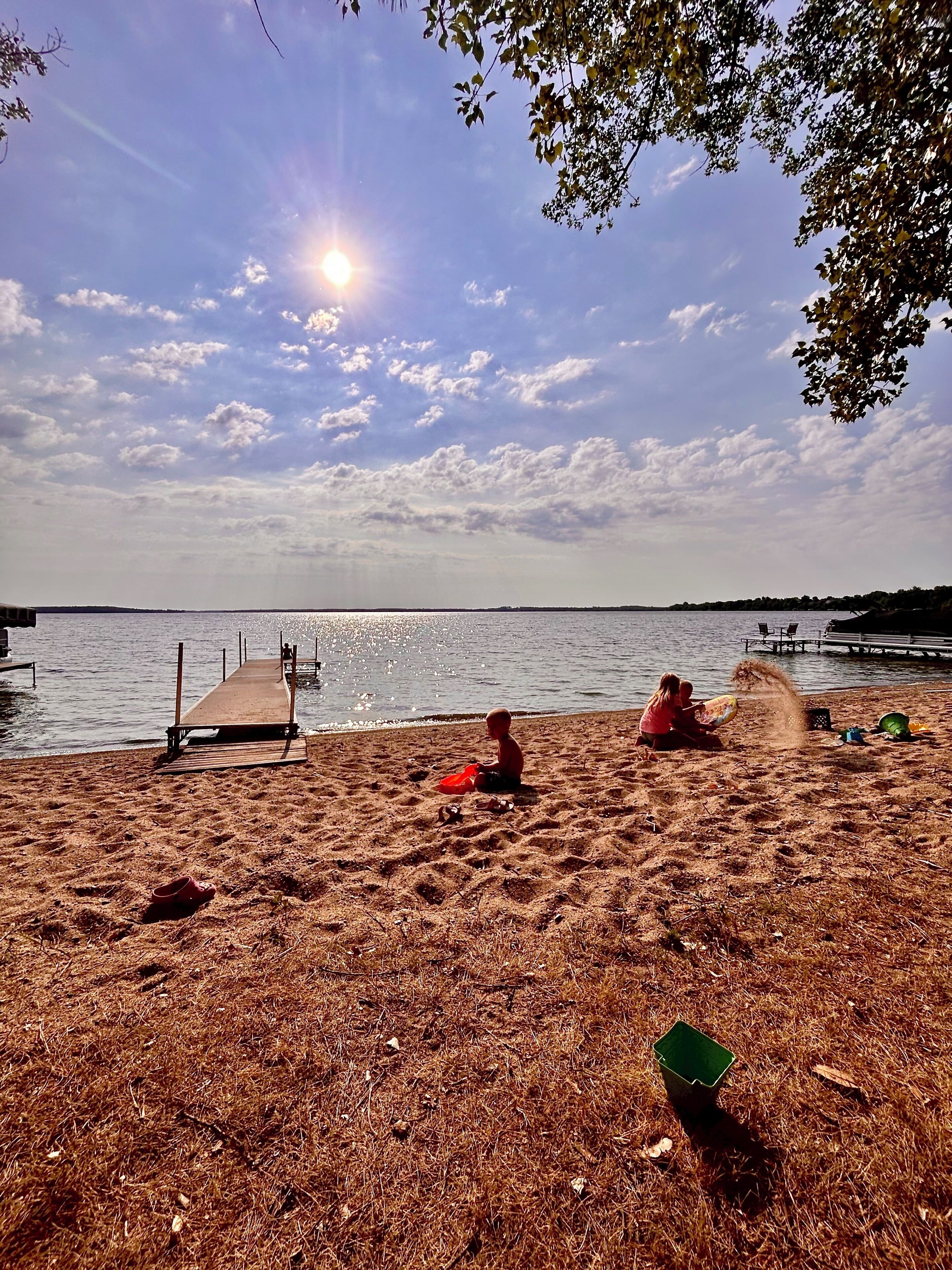 A beach with a wooden pier extending into calm water, a clear sky, and a few scattered clouds.