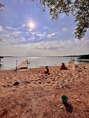 A beach with a wooden pier extending into calm water, a clear sky, and a few scattered clouds.