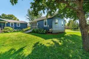 A residential property with a well-maintained lawn, a small house with a porch, and a mature tree providing shade.