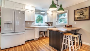A modern kitchen with white cabinets, a central island with stools, a refrigerator, and a water dispenser.