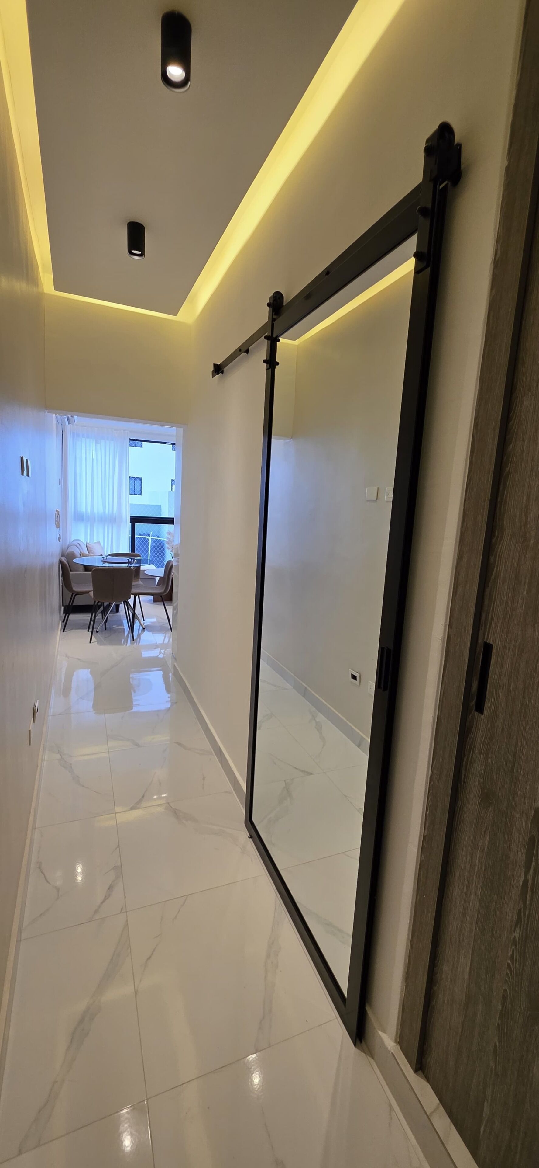 Un couloir avec une porte coulissante, un coin repas avec une table et des chaises, et une vue sur une autre pièce.