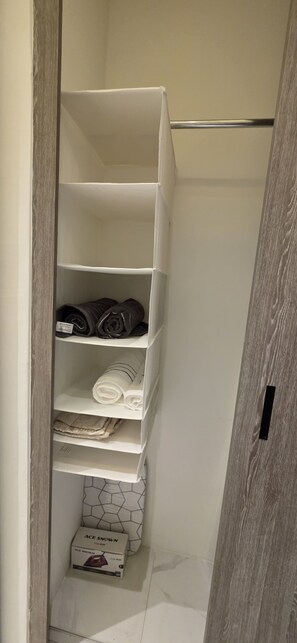 Ein weißer Schrank mit Regalen, gefüllt mit gefalteten Handtüchern und einer Kiste mit dem Aufdruck 'ACE SNOWN'.