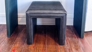 Eine dunkelblaue Bank mit gepolstertem Sitz und zwei Schubladen, vor einem Wandbehang aus Makramee platziert.