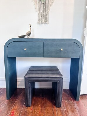 Eine dunkelblaue Bank mit gepolstertem Sitz und zwei Schubladen, vor einem Wandbehang aus Makramee platziert.