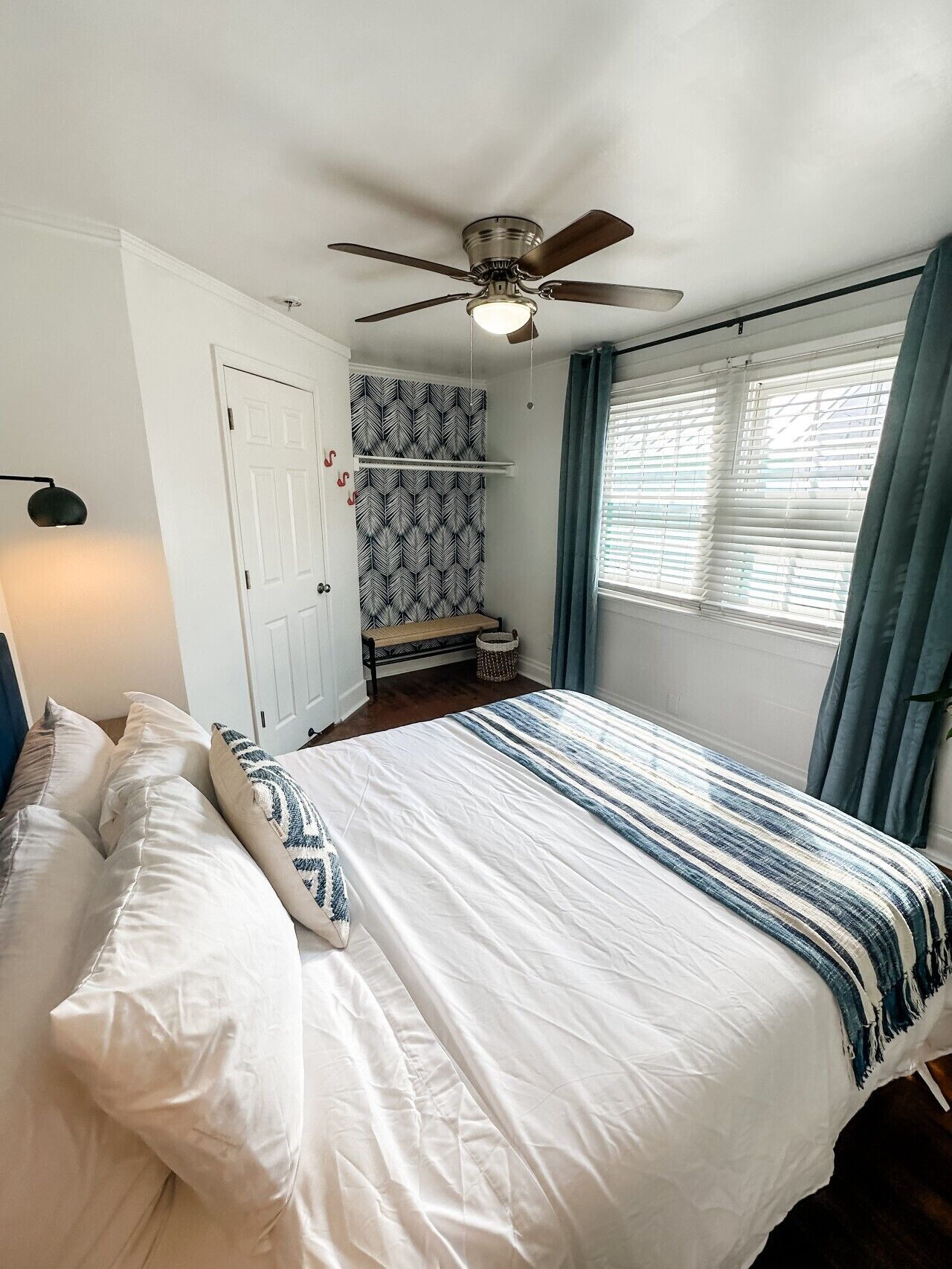 A bedroom with a bed, a ceiling fan, a window with curtains, and a patterned wall.