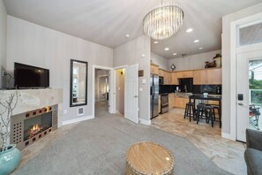 A modern living room with a fireplace, a television, and a chandelier. - Steps to Beach + Downtown, Oceanview | Full Duplex (Rockaway Beach)