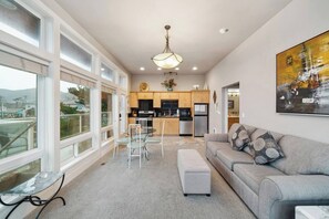 A modern living room with a grey sofa, a glass coffee table, and a dining area with a white table and chairs. - Steps to Beach + Downtown, Oceanview | Full Duplex (Rockaway Beach)