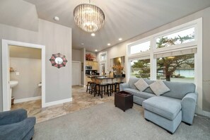 A modern living room with a grey sofa, a coffee table, and a chandelier. - Steps to Beach + Downtown, Oceanview | Full Duplex (Rockaway Beach)