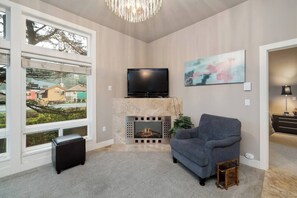 Ein Wohnzimmer mit Kamin, Fernseher und großem Fenster mit Blick auf eine Wohngegend.