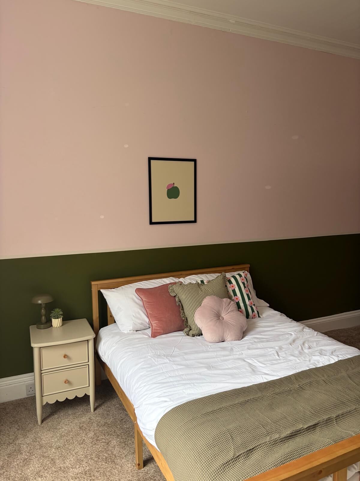 Une chambre à coucher avec un lit, une table de chevet, un tableau encadré au mur et un mur vert.