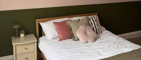 A bedroom with a bed, a nightstand, a framed picture on the wall, and a green wall.